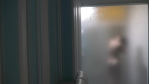 Woman behind blurry glass. Girl preparing take shower. Woman in bathroom. a man watches as a woman takes a shower through a glass wall in the shower. 4k