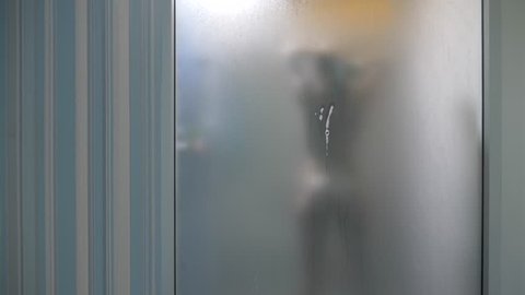 Woman behind blurry glass. Girl preparing take shower. Woman in bathroom. a man watches as a woman takes a shower through a glass wall in the shower. 4k