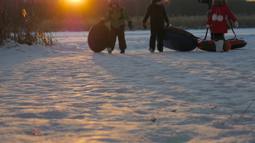 Winter vacation: kids riding on inflatable snow tube from a hill. Children climb the hill, carrying a sled. Winter, active rest.
