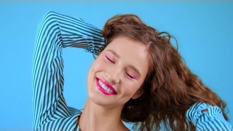 Close-up portrait: happy beautiful young girl with long hair is having fun playing with her hair and laughing. Girl model on a colored background corrects hair grimaces, rejoices, smiles. Slow motion,
