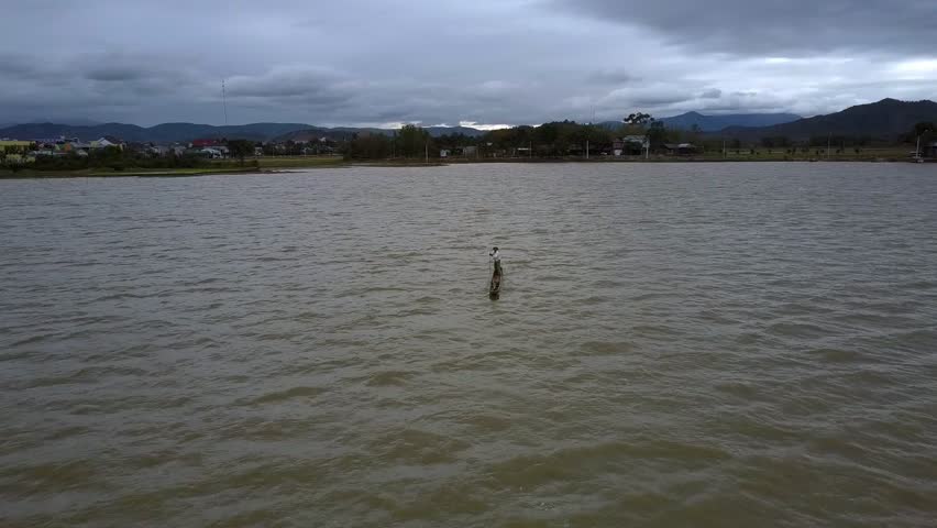 upper view peasant drifts in pirogue on large rippling lake removing from bank hill silhouettes against overcast sky