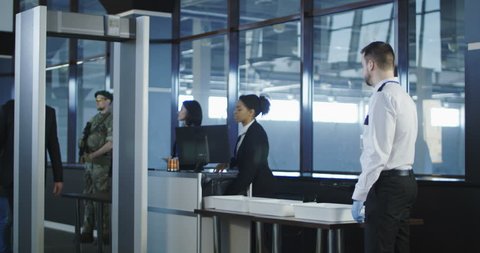 Airport security agent using a metal detector on a male passenger in a suit to pat him down at the boarding gate after passing through the x-ray scanner. 4K shot on Red cinema camera.