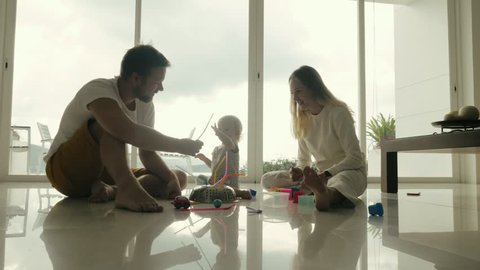 Family couple mom and dad playing with little girl on floor in room interior with panoramic window. Young mother and father having fun leisure time together little daughter