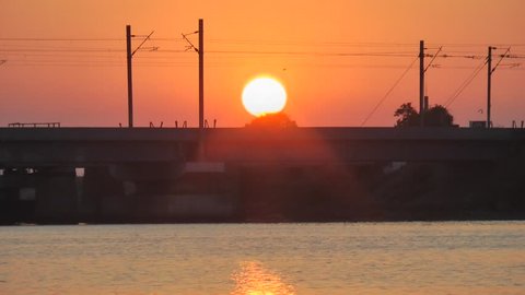 During Sunset A Train Crossing Creek Bridge At Ennore, North Chennai, Tamil Nadu, India With Yellowish Background and Golden Water Foreground