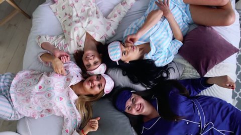 Four smiling women in pajamas lie on the bed and look directly into the camera at a pajama party. bridesmaid. Bachelorette. Cheerful and joyful.