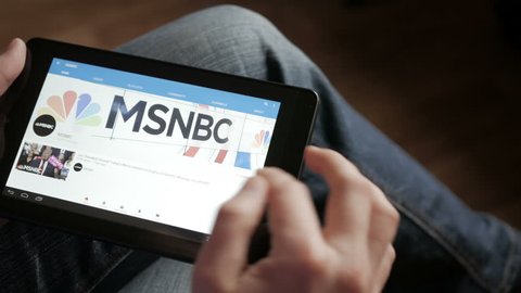 Man using youtube app on tablet computer device, scrolling videos, tapping on play button. Closeup. Shot over shoulder. MSNBC News live.  4K UHD. LOS ANGELES - Mart 2018.