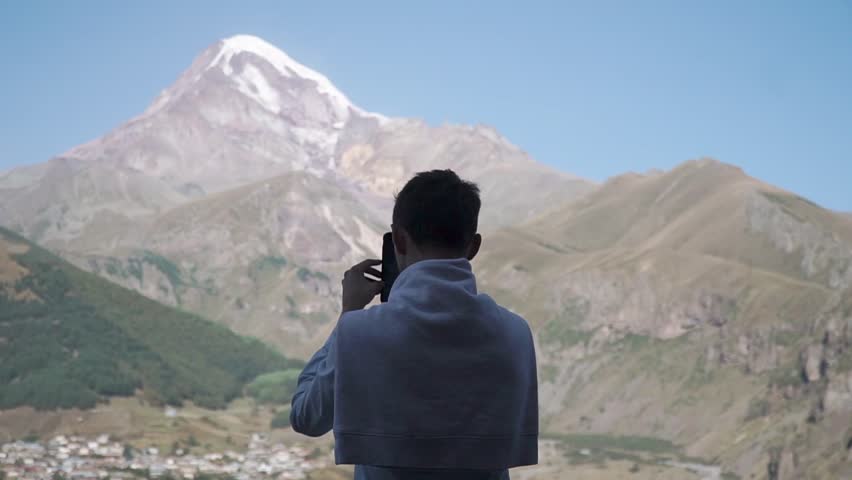Man takes a photo on his smartphone looking at beautiful Georgian mountains