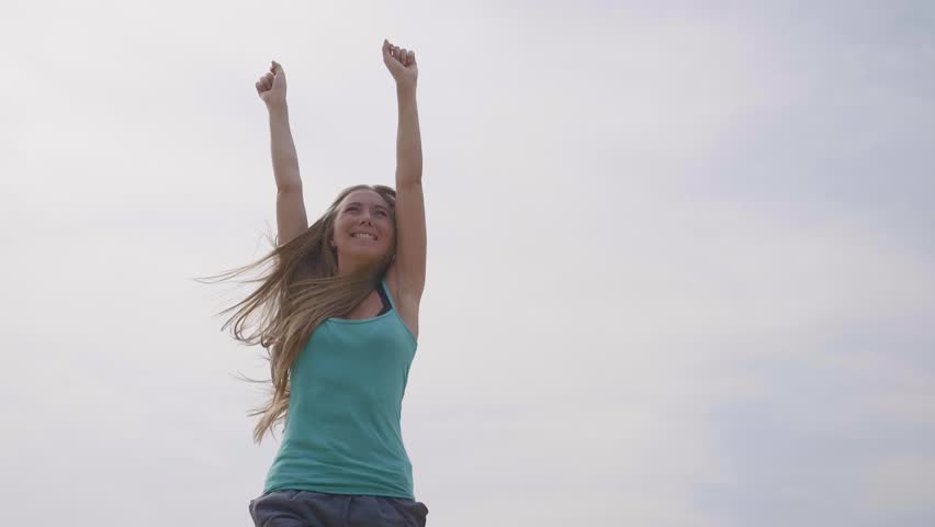 Young happy woman raising hands up and jumping high in the sky. Freedom, happiness,healthy and active lifestyle concept.