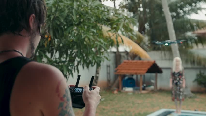 Group of happy people: girls of different races and one guy pilot to the drone, which is flying over them, operated by the bearded guy and capturing video