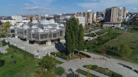 PRISTINA, KOSOVO - OCTOBER 2017: Low angle drone flight past iconic National Library of Kosovo building, revealing abandoned Serbian Orthodox church in Pristina, education and architecture Kosovo