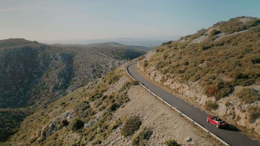 Amazing breathtaking and inspiring to travel and adventure landscape of small mountain road winding in sunset, aerial drone shot of small red cabriolet convertible car explore destination for summer Royalty-Free Stock Footage #1008626791
