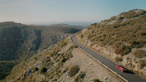 Amazing breathtaking and inspiring to travel and adventure landscape of small mountain road winding in sunset, aerial drone shot of small red cabriolet convertible car explore destination for summer