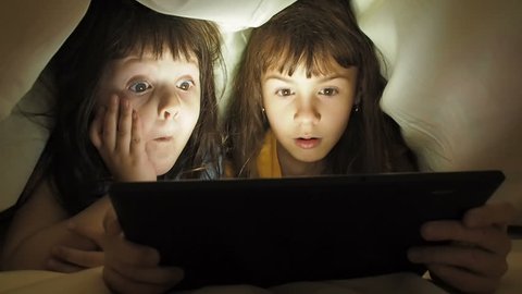 Children with a tablet under the blanket. Children at night with a tablet. Little girls with a tablet in the bedroom. digital addiction