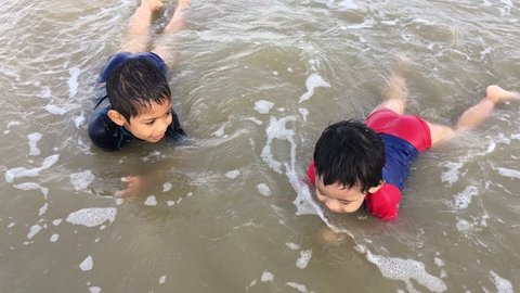 A happy little brothers from Southeast with swimming suit playing together at the beach during weekend.
