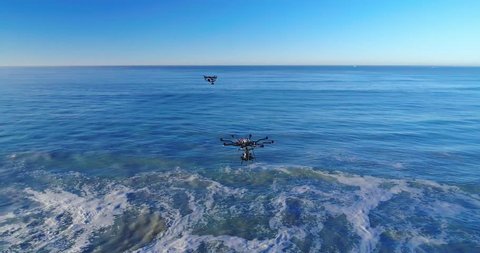 Aerial view of a drone orbiting two drones over the ocean at the beach on a sunny day. 4K