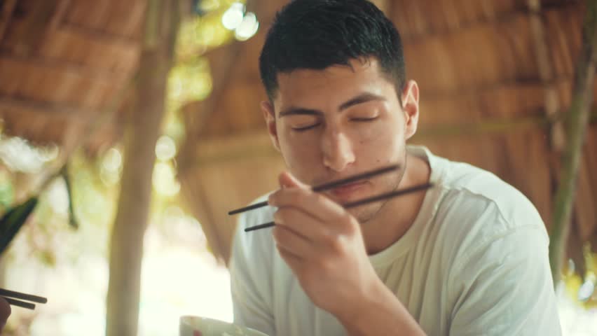 Handsome young man enjoying a bowl of rice while on vacation in Ho Chi Minh City and looks at the camera in slow motion