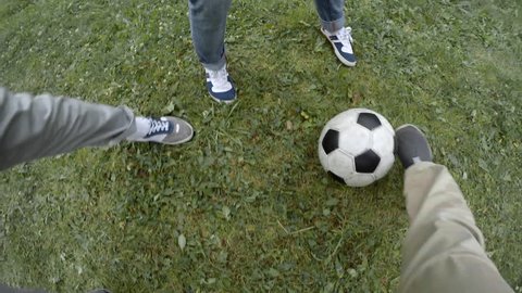 Point of view shot of primary school boy dribbling ball when playing football with friends, some of them falling down