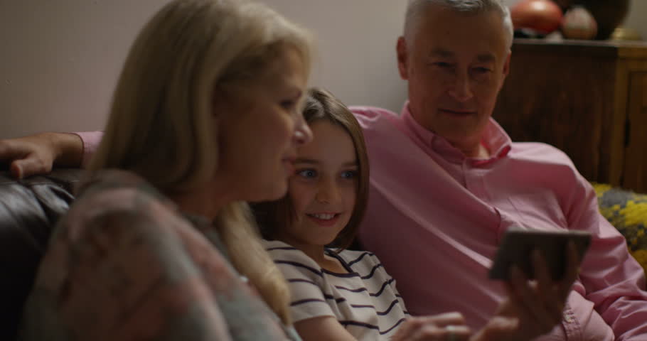 4K Happy mature couple with granddaughter, watching digital media on smartphone. Slow motion.