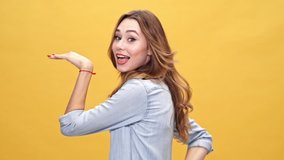 Funny brunette woman in denim shirt dancing and looking at the camera over yellow background
