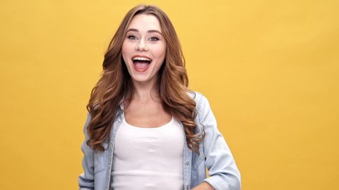 Funny brunette woman in denim shirt amusing and looking at the camera over yellow background
