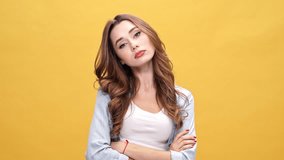 Upset offended brunette woman in denim shirt turning away with crossed arms over yellow background