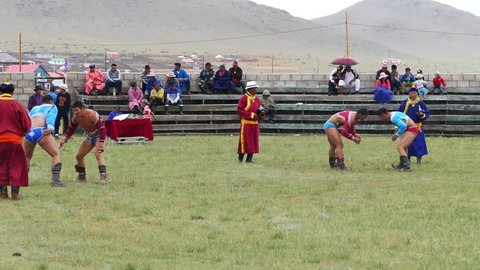 Telmen sum, Mongolia - July 15, 2017: Mongolian national holiday Naadam. Two pairs of wrestlers compete against each other in an open stadium. The spectators in the stands watch the fight.