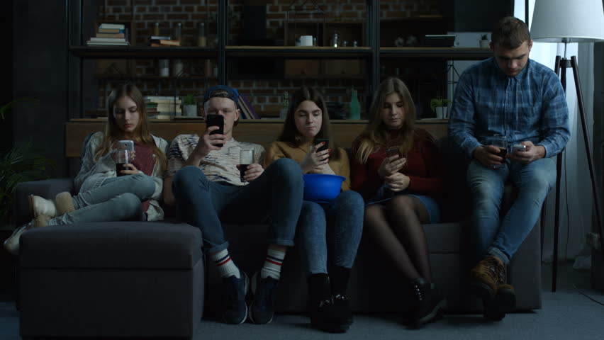 Group of young friends phubbing each other while sitting in a row on the couch in domestic room. Busy teenagers using smart phones with disinterest on each other. Technology and smart phone addiction. Royalty-Free Stock Footage #1008668863