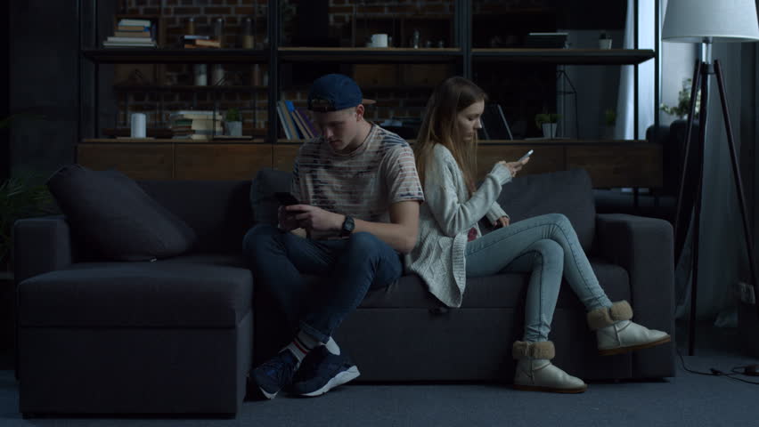 Attractive young couple sitting back to back at home on couch obsessed with smartphones. Couple with mobile phones ignoring each other as strangers, communication problems and social network addiction Royalty-Free Stock Footage #1008668881