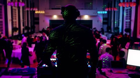 Unrecognizable Rear view of DJ mixing dancing in front his turntables and mixer and laptop during party wedding - illumination with laser light of his back and large room with guests