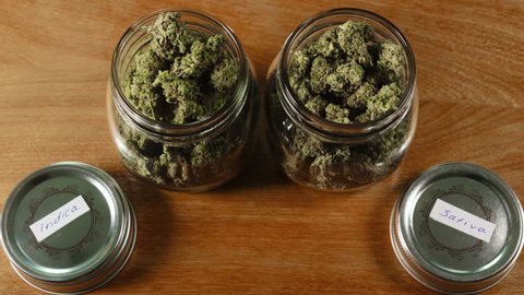 Jar of Sativa Cannabis and a jar of Indica Cannabis on wood table