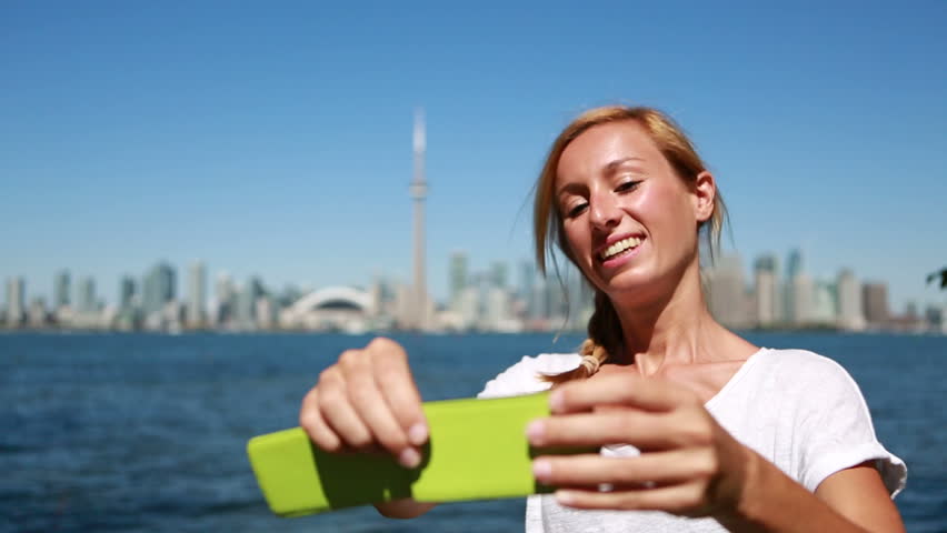 Young woman travelling in Canada takes selfies in Toronto. Woman taking selfie wile travelling, Toronto skyline in the background 