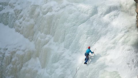 Ice Climbing Frozen Waterfall. Climbing Alpinism Winter.  Climber climbs on icy wall with wind and snow blowing. A man climbing a frozen waterfall. Climbing gear. 