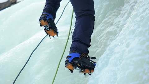 Ice Climbing Frozen Waterfall. Climbing Alpinism Winter.  Climber climbs on ice wall with wind and snow blowing. A man climbing a frozen waterfall. Climbing gear. 
