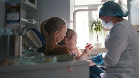 Girl, her mom and the dentist in the dental office, the stomatologist advising with a special toy