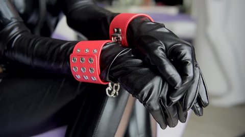 Woman in black outfit with red cuffs close-up. Female hands in leather gloves and handcuffs.