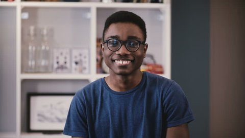 Portrait of African American college student. Happy black young guy in glasses smiles, then becomes serious. Emotions 4K