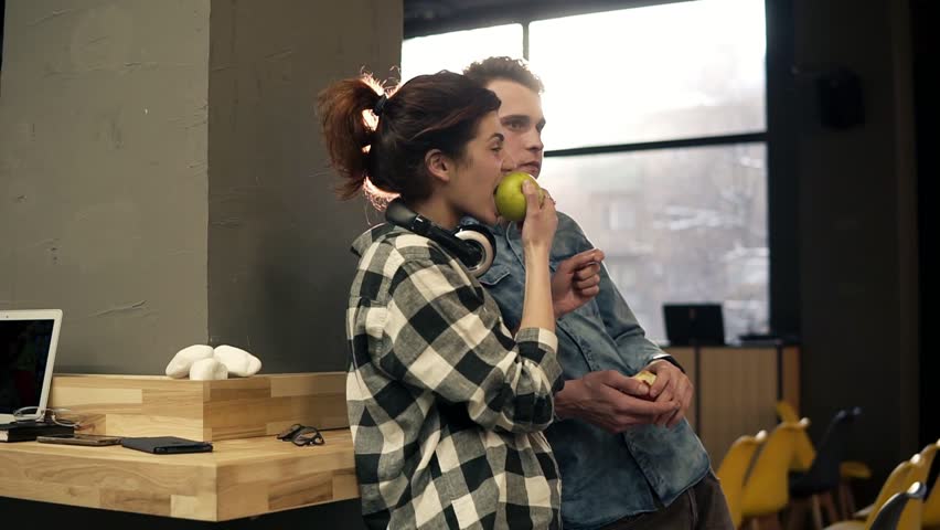 Couple of two young happy people having fun time together, eating apples and enjoying their lives. Urban hipster outfits. Youth, millenial generation.