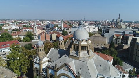 NOVI SAD, SERBIA - OCTOBER 2017: Close drone flight past dome of Jewish synagogue, with church towers and skyline of Novi Sad city, Serbia