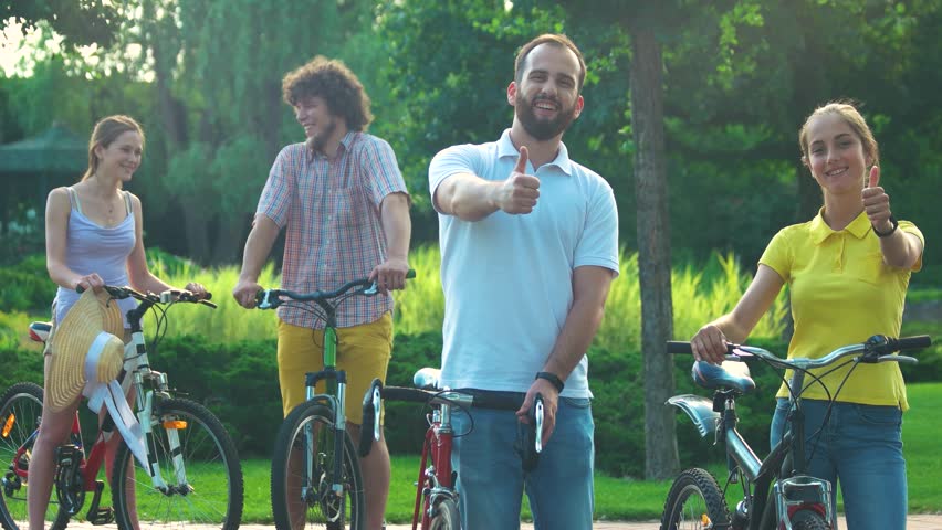 Couple of young cyclists showing thumbs up. Happy cheerful young man and woman with bicycles outdoors. Happy vacation together.