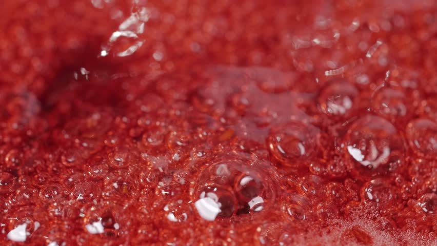 Bubbles rising in thick, red liquid making an abstract background. Macro shot of a cranberry jam. Royalty-Free Stock Footage #1008725555