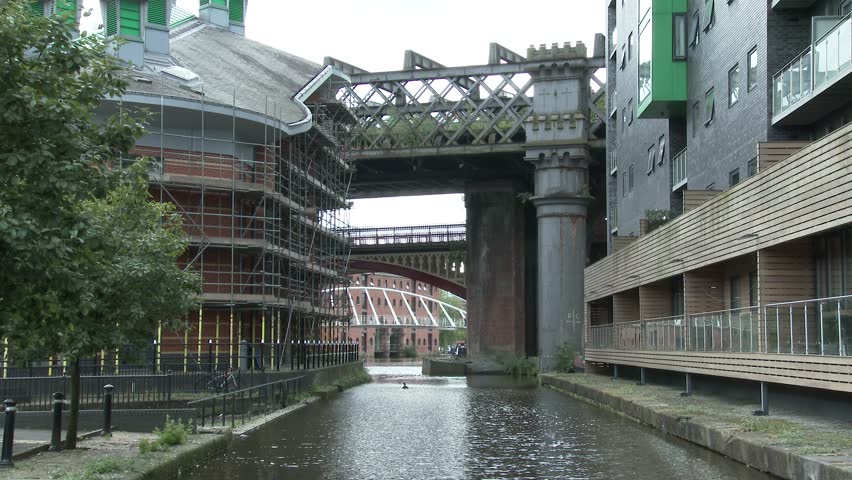 An inlet of the Bridgewater Canal at its Castlefield terminus in Manchester, crossed by rail bridges and flanked by new development buildings.  
