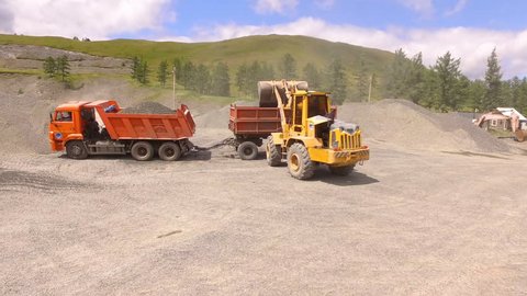 AERIAL: The excavator loads the crushed stone in a truck with a semitrailer. Quarry for the extraction of gravel. Production, transportation.