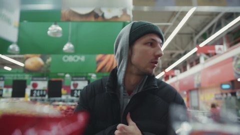 Portrait man steals nuts looks around and go away in supermarket shoplifting 