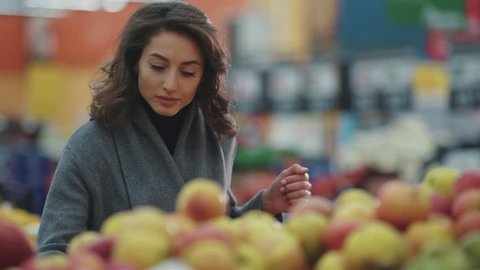 Serious young woman choosing apple at fruit vegetable supermarket marketplace lifestyle commerce product fresh hand customer food beautiful girl shopping selecting face buy store grocery holding