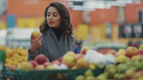 Attractive young woman choosing apple at fruit vegetable supermarket marketplace 
