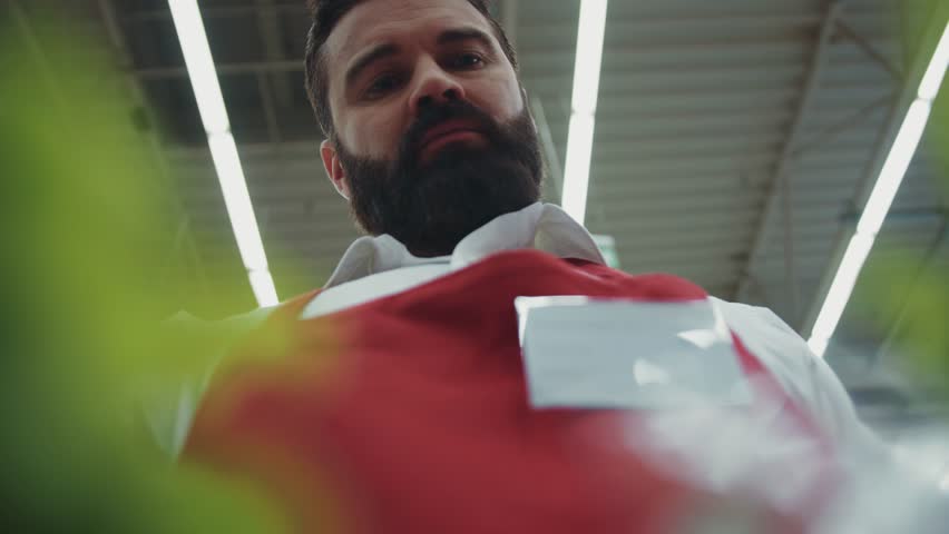 Close up frame from below serious young seller man with beard work in supermarket shop 