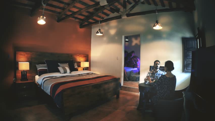 Couple celebrating anniversary in a hotel suite and toasting with red wine 