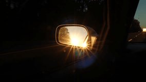 Bright fiery orange sunburst from the sunset reflected in a side mirror of a car driving slowly along a rural motorway