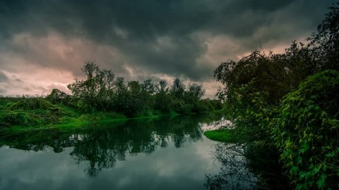 Cinemagraph of a slow river flowing as dark, dramatic storm clouds form overhead in a seemless and endless time lapse