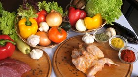 Different types of meat lie on wooden boards on the background of vegetables of lettuce leaves, spices, curry, paprika, a slow passage of the video from above. Side view.